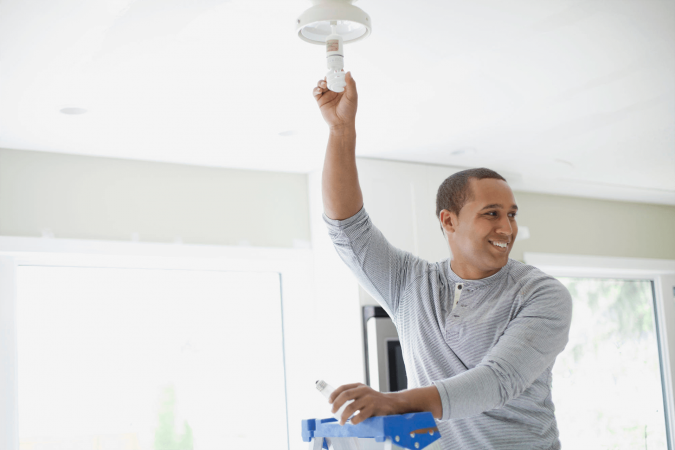 tips to save on electric costs during summer man changing light bulb
